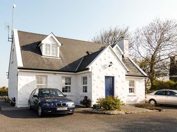 a white house with a car parked in front of it at Brandy Harbour Cottage in Kilcolgan