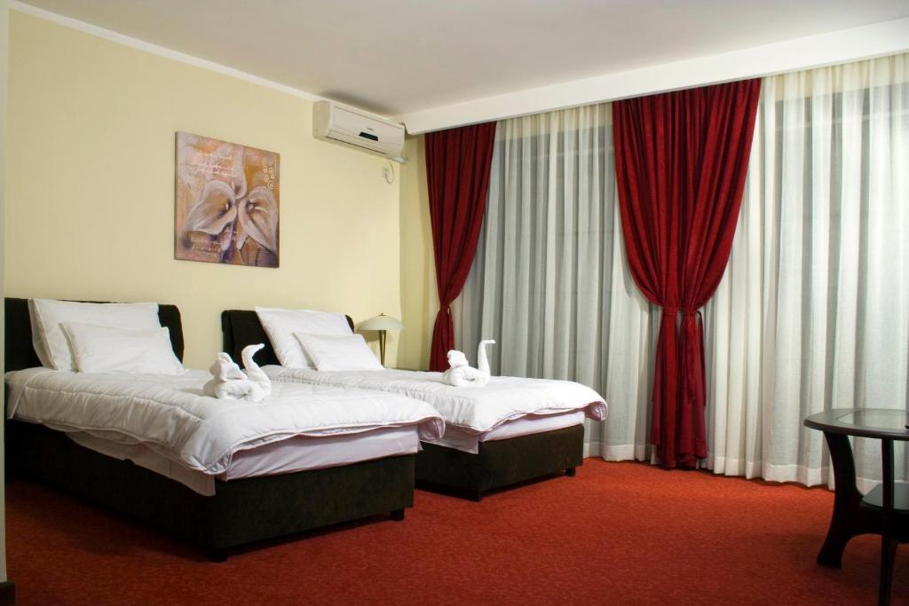 two beds in a hotel room with red curtains at Vila Prica in Niška Banja