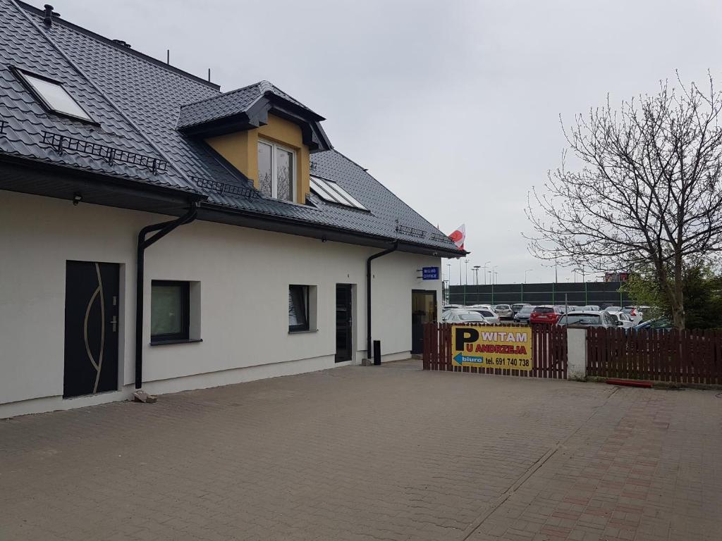 a white building with a fence next to a parking lot at Noclegi i Parking u Andrzeja in Gdańsk