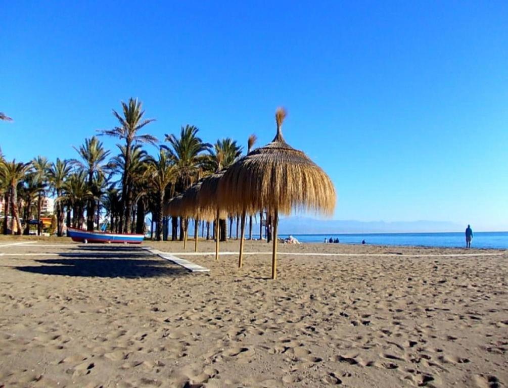 a beach with a straw umbrella and palm trees at Bellamar in Torremolinos