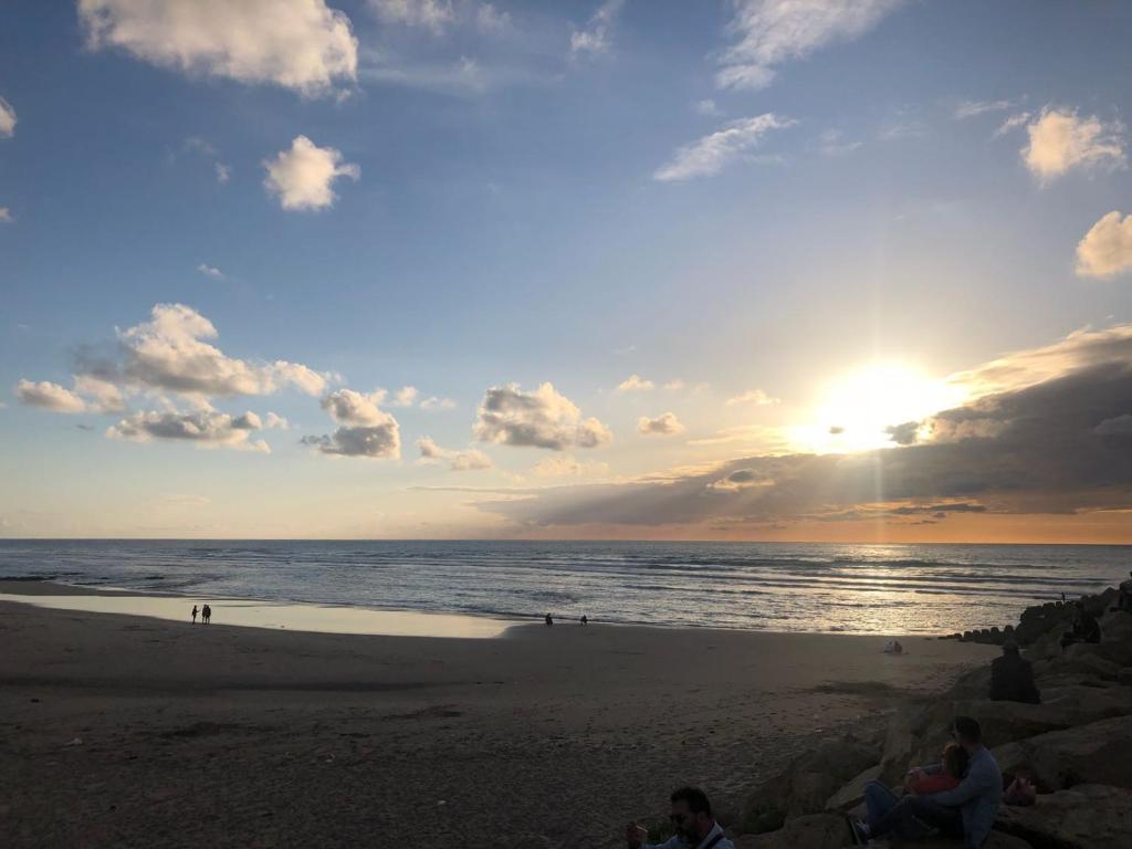 a group of people sitting on the beach at sunset at Marina Golf Appart Chez Hicham in Asilah