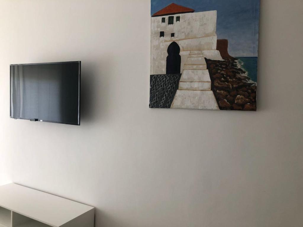 a tv on a wall with a painting of a person at Marina Golf Appart Chez Hicham in Asilah