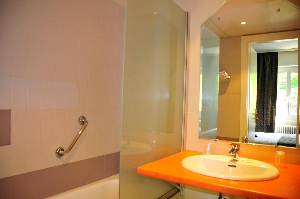 a bathroom with a sink and a tub and a mirror at Hôtel aux Bruyères in Orbey