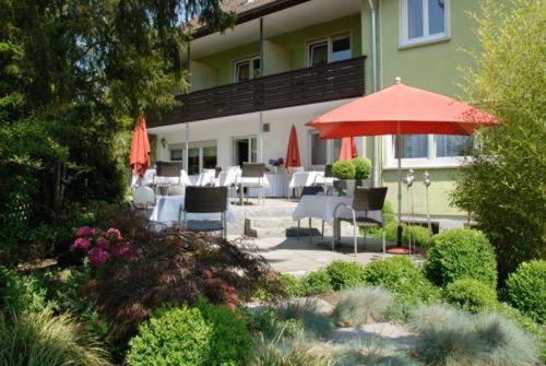 eine Terrasse mit einem roten Sonnenschirm, Stühlen und Tischen in der Unterkunft Gästehaus Schlegel in Stetten