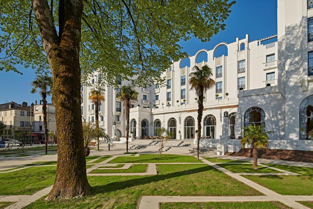 un gran edificio blanco con palmeras delante en Hotel & Spa Vacances Bleues Le Splendid, en Dax