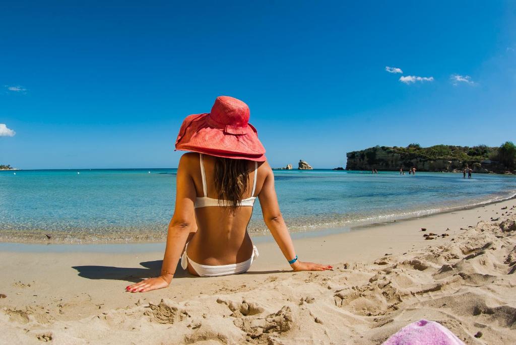 Futura Club Spiagge Bianche في فونتاني بيانكي: امرأة ترتدي قبعة جالسة على الشاطئ