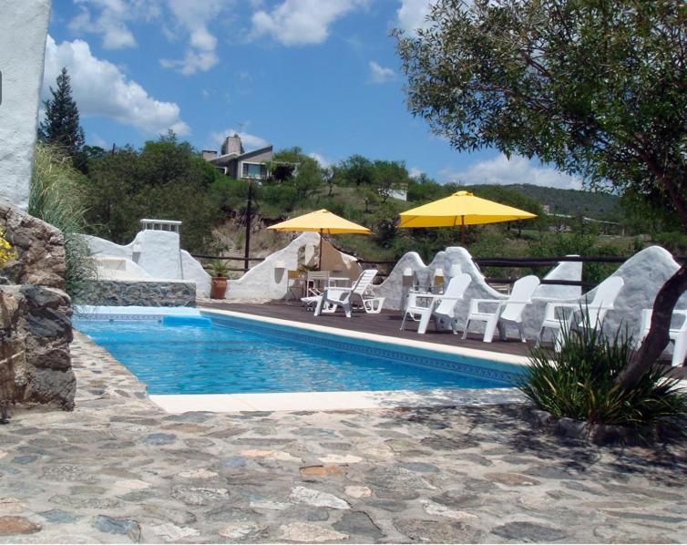 una piscina con sillas blancas y sombrillas junto a ella en Soles Blancos Serranita en Alta Gracia
