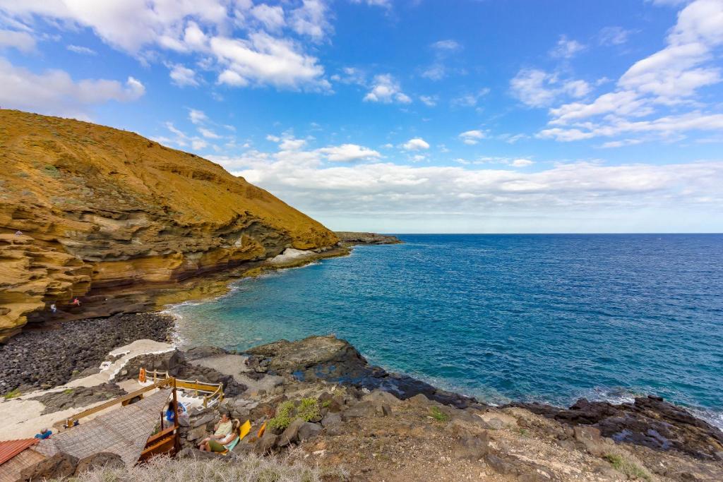 um grupo de pessoas em pé nas rochas perto do oceano em Tenerife Montaña Amarilla em Las Galletas