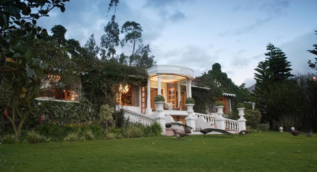 a large white house with a staircase in a yard at La Mirage Garden Hotel & Spa in Cotacachi