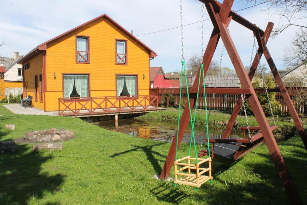 a yellow house with a swing in front of it at Viesu nams AMRAI in Ventspils