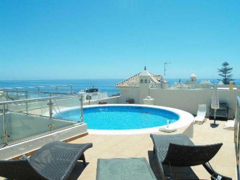 a swimming pool with chairs and the ocean in the background at Maravilloso apartamento in Nerja