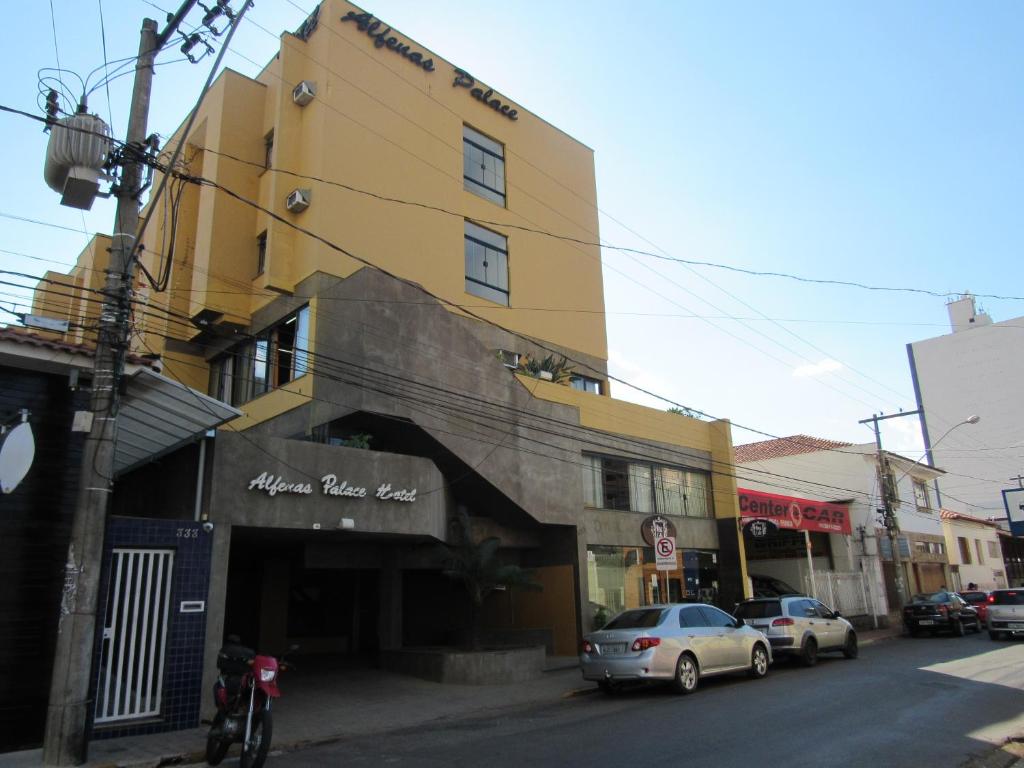 Alfenas Palace Hotel في ألفيناس: مبنى أصفر على شارع المدينة مع سيارات متوقفة