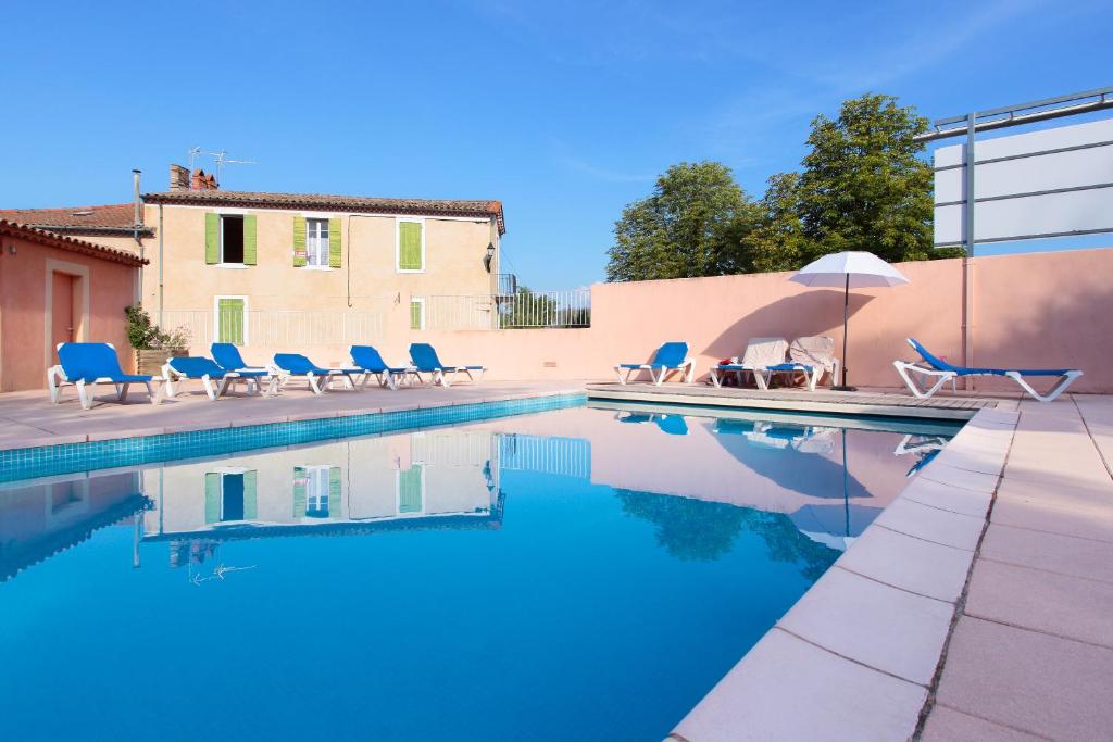 - une piscine avec des chaises et un parasol à côté d'un bâtiment dans l'établissement Les Colonnes, à Gréoux-les-Bains