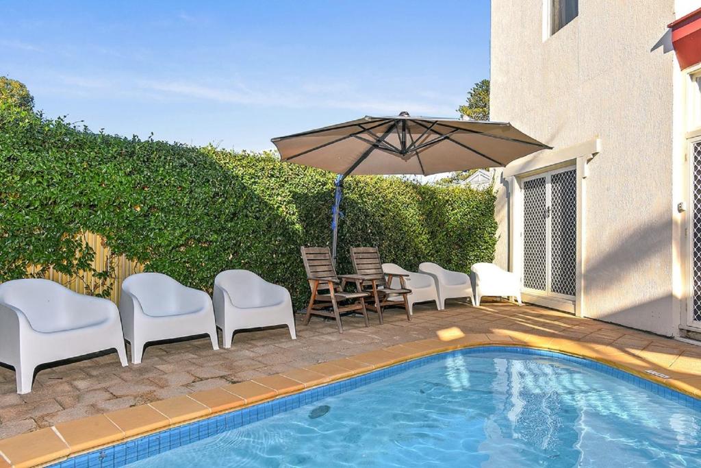 un patio con sillas y una sombrilla junto a la piscina en Smugglers Resort-Style Apartments no 9, en Victor Harbor