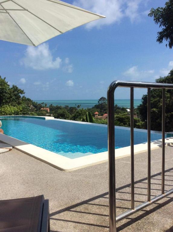 a swimming pool with an umbrella and the ocean at Samui Grand Rock in Lamai