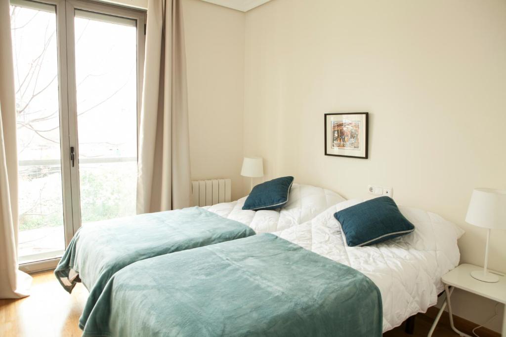 a white bedroom with two beds and a window at Piso en el Centro Plaza de España in Seville