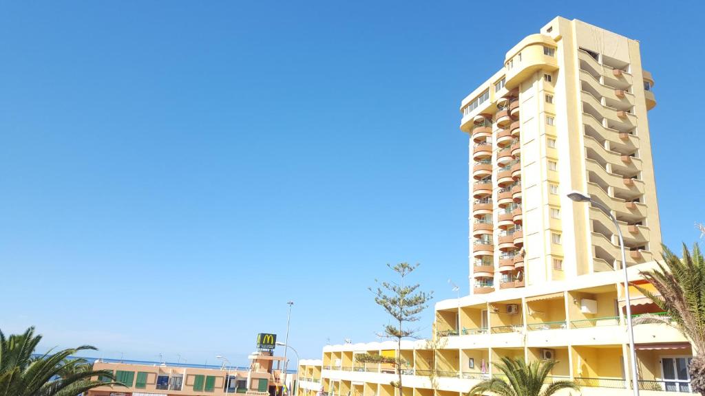 a tall white building with palm trees in front of it at Torres del Sol Playa de Las Vistas FREE WIFI in Playa de las Americas