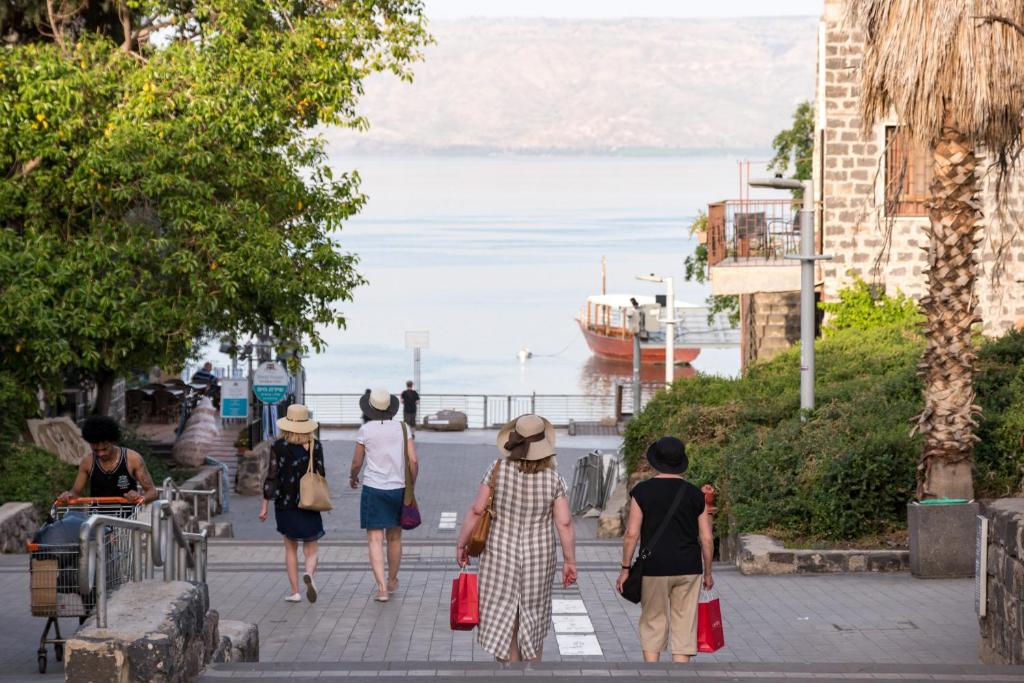 a group of people walking down a sidewalk looking at the ocean at Kinneret Lodging in Tiberias