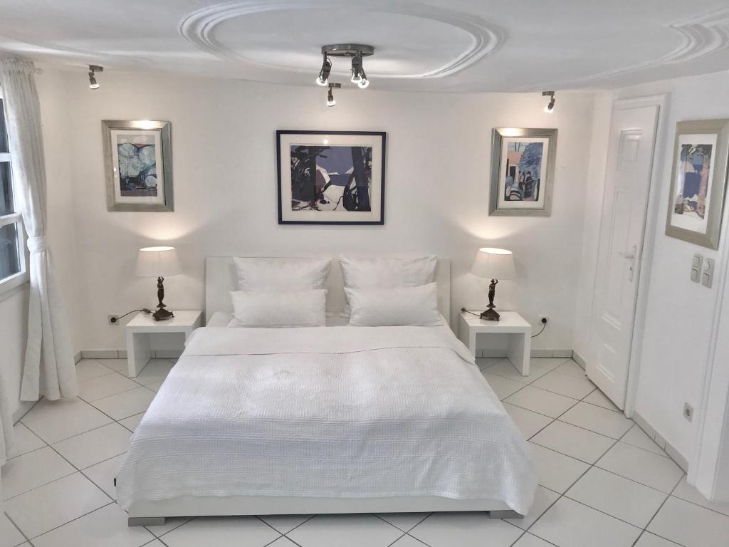 a white bedroom with a large white bed and two tables at Kramwinkelsuite Regensburg in Regensburg