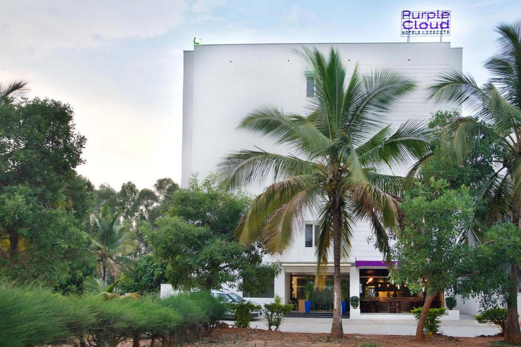 a white building with a palm tree in front of it at Purple Cloud Hotel in Devanahalli-Bangalore