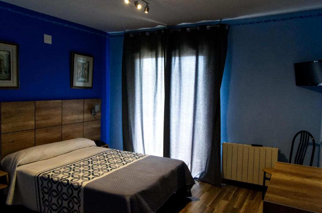 een slaapkamer met blauwe muren en een bed en een raam bij Hotel Don Angel in Villanueva de la Cañada