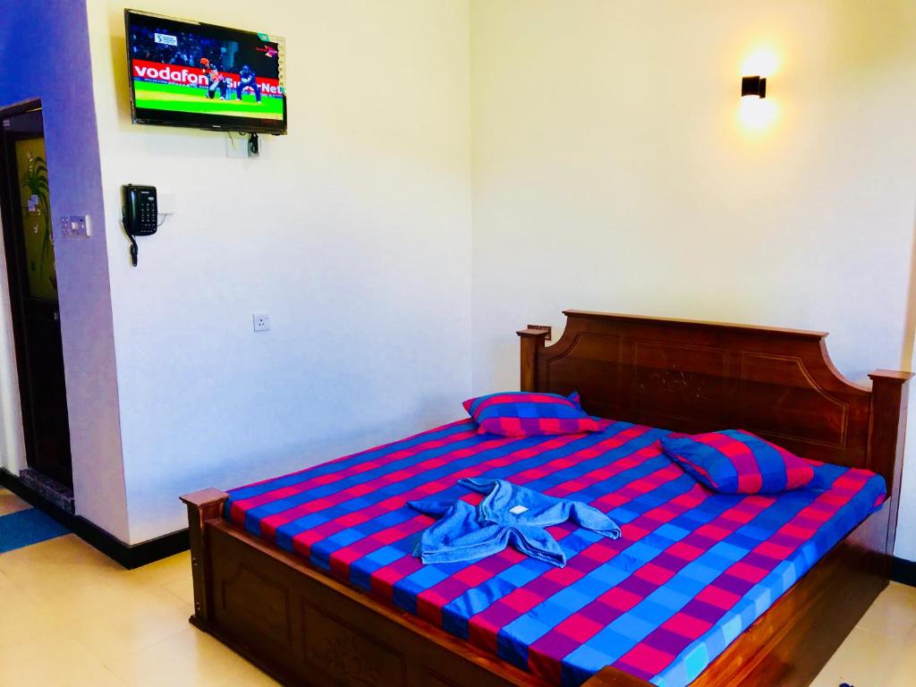 a bed with a red and blue checkered sheets and a television at Travellers Halt in Ratnapura