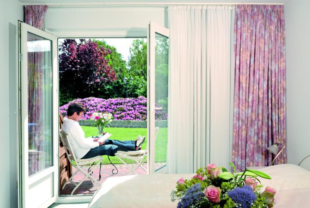 a man sitting in a chair on a patio with a window at Hotel garni Haus am Meer in Neuharlingersiel