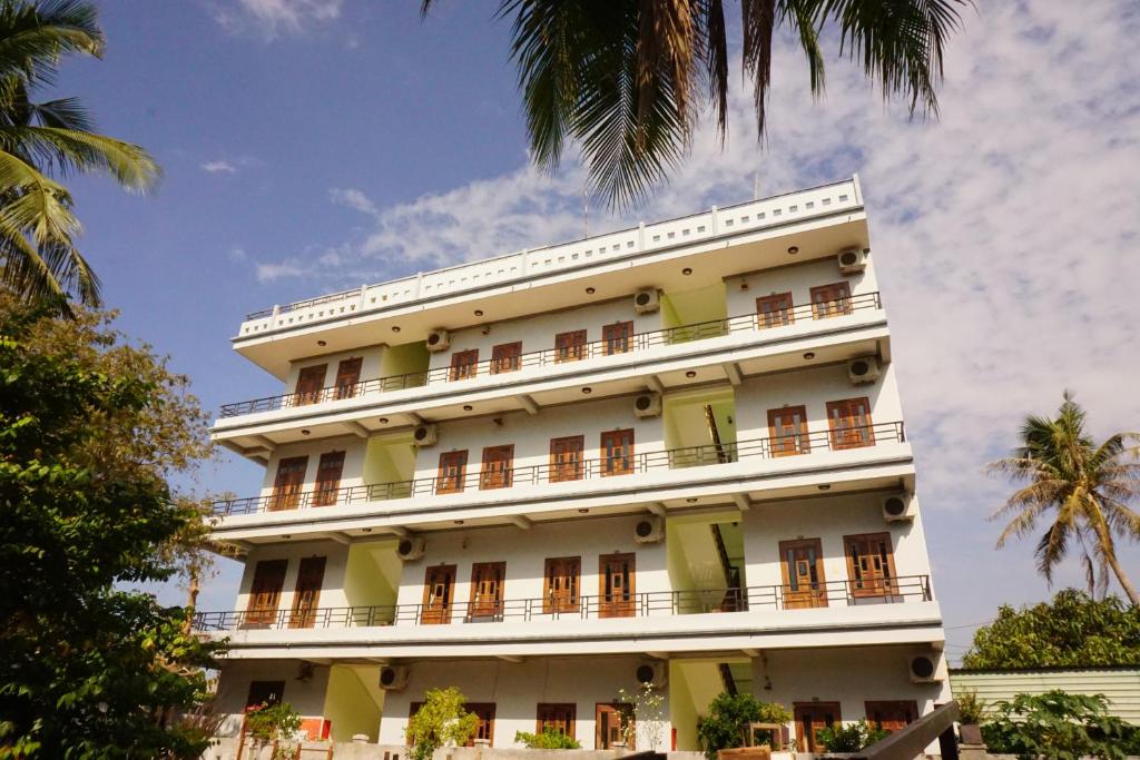a tall white building with windows and palm trees at Cat Tien Guesthouse in Mui Ne