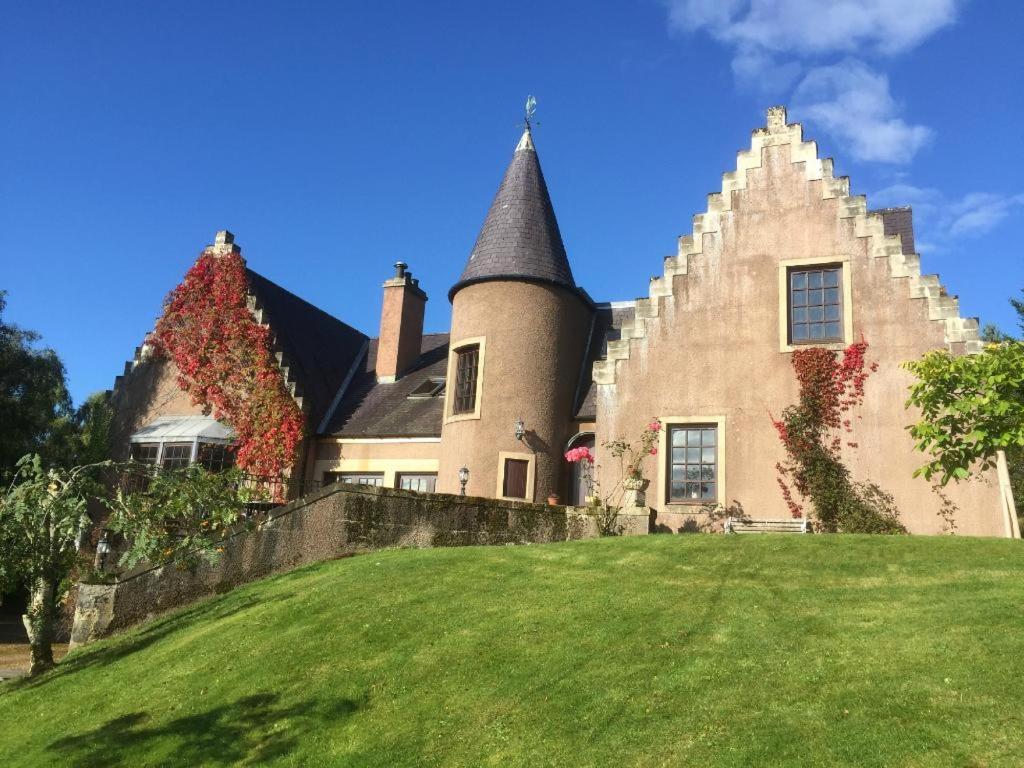 a large house with a turret on a green lawn at Highland Bear Lodge & Luxury Bear Huts in Drumnadrochit
