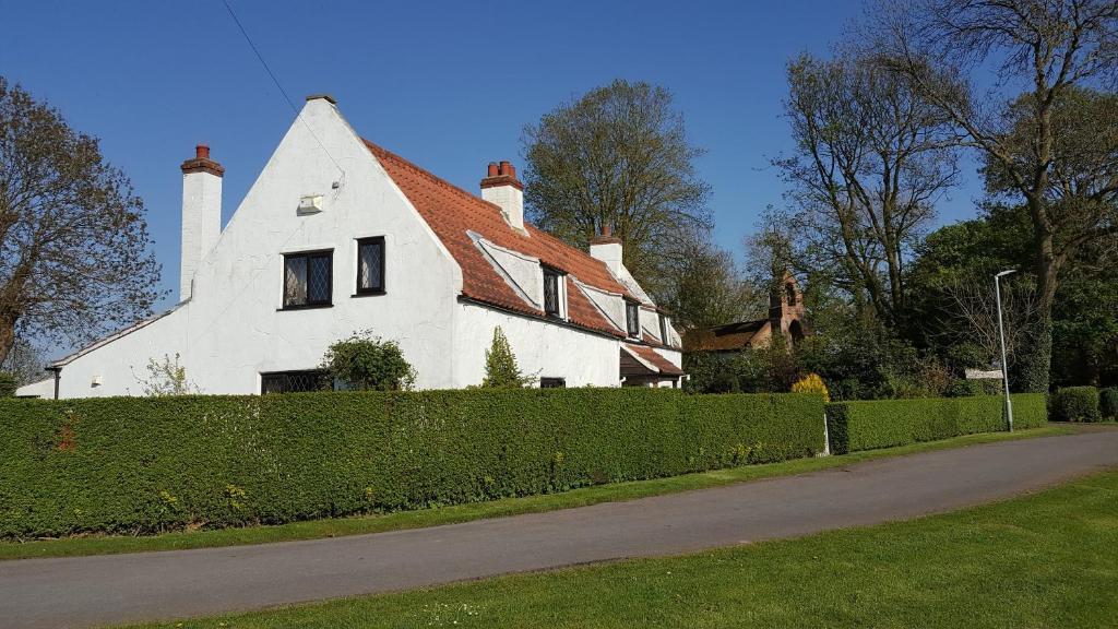 a white house with a hedge in front of a street at Wickham House in North Somercotes