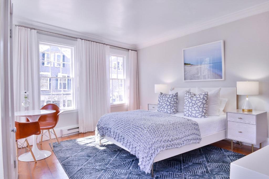 a bedroom with a bed and a desk and two windows at Hotel Pippa in Nantucket