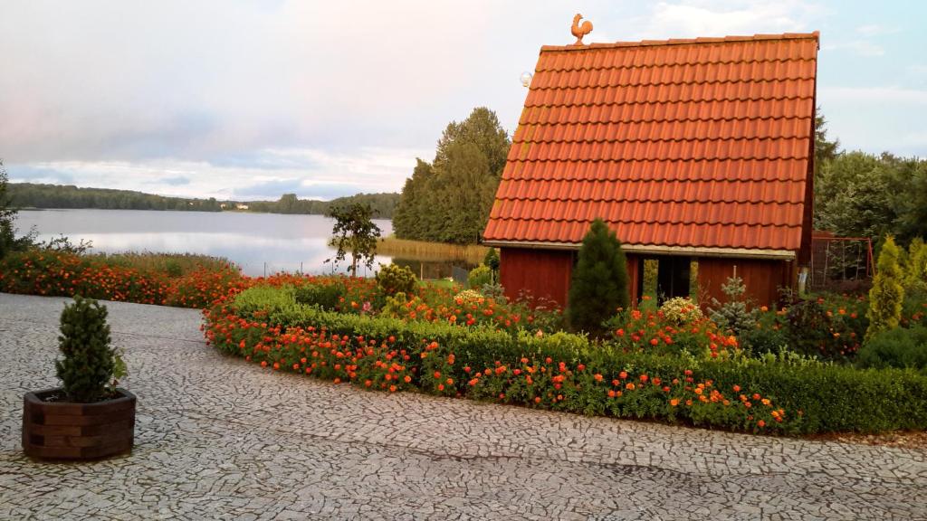 コシチェジナにあるAgroturystykaの花の咲く庭園の隣にあるオレンジ色の屋根の家