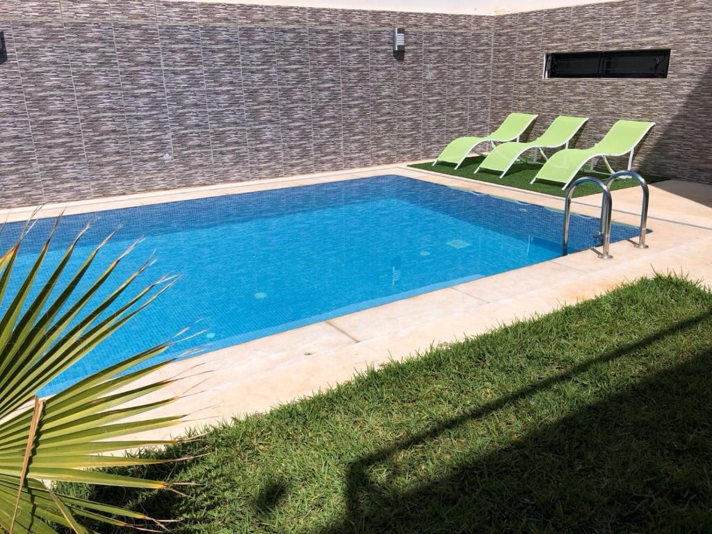 - une piscine avec des chaises vertes à côté d'un bâtiment dans l'établissement Villa Nour, à Fès