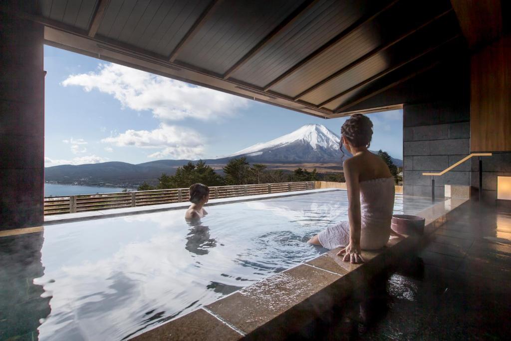 due donne sedute in una piscina con una montagna sullo sfondo di Hotel Mt. Fuji a Yamanakako