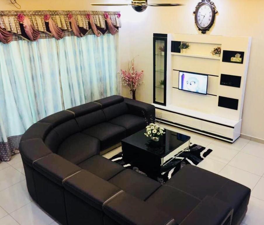 a living room with a black couch and a tv at Bukit Banyan Homestay Sungai Petani in Sungai Petani