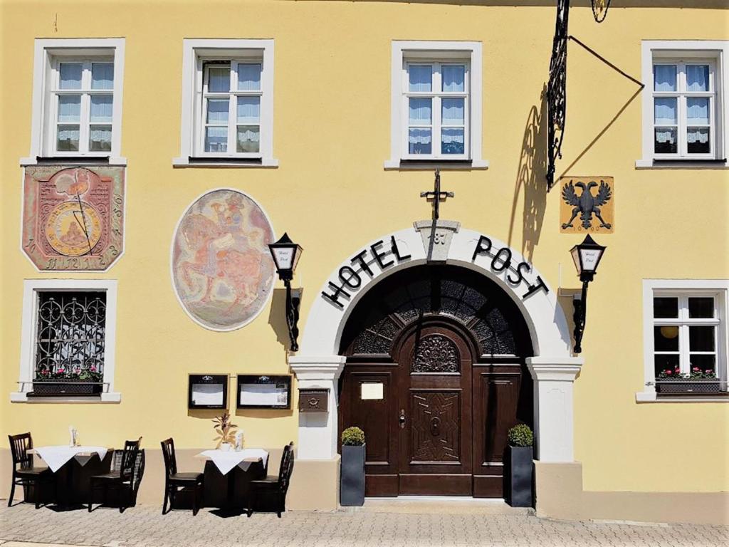 a yellow building with a wooden door and tables and chairs at Garni Hotel Post in Weißenstadt