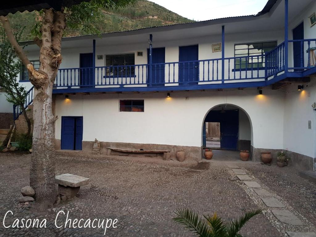a white building with a blue balcony and a tree at Casona Checacupe in Checacupe