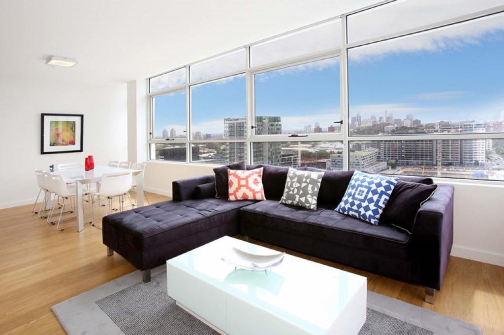 a living room with a black couch and a table at Gadigal Groove - Modern and Bright 3BR Executive Apartment in Zetland with Views in Sydney