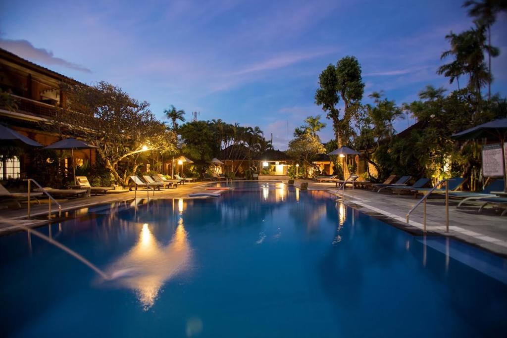 a large swimming pool with blue water at night at Bumi Ayu Bungalow Sanur in Sanur