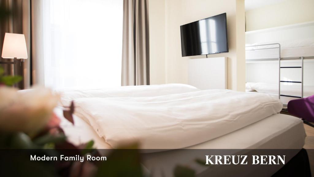 a bedroom with a bed with white sheets and a tv at Kreuz Bern Modern City Hotel in Bern