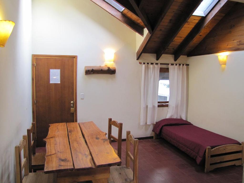 a room with a wooden table and a bed at Hostel La Angostura in Villa La Angostura