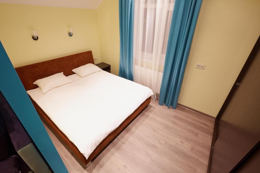 Un pequeño dormitorio con una cama blanca y cortinas azules en Apartment Fedkovycha, en Leópolis