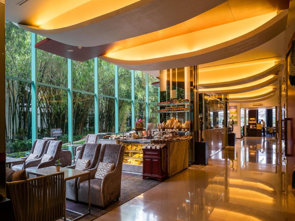 A bright hotel lounge and bar sit beneath sweeping amber-lit ceiling panels.