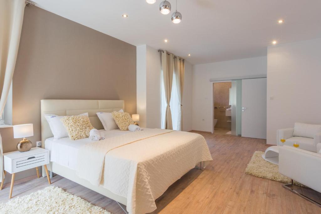 um quarto com uma grande cama branca e uma cadeira em Rooms Sea & Sun with private parking em Zadar