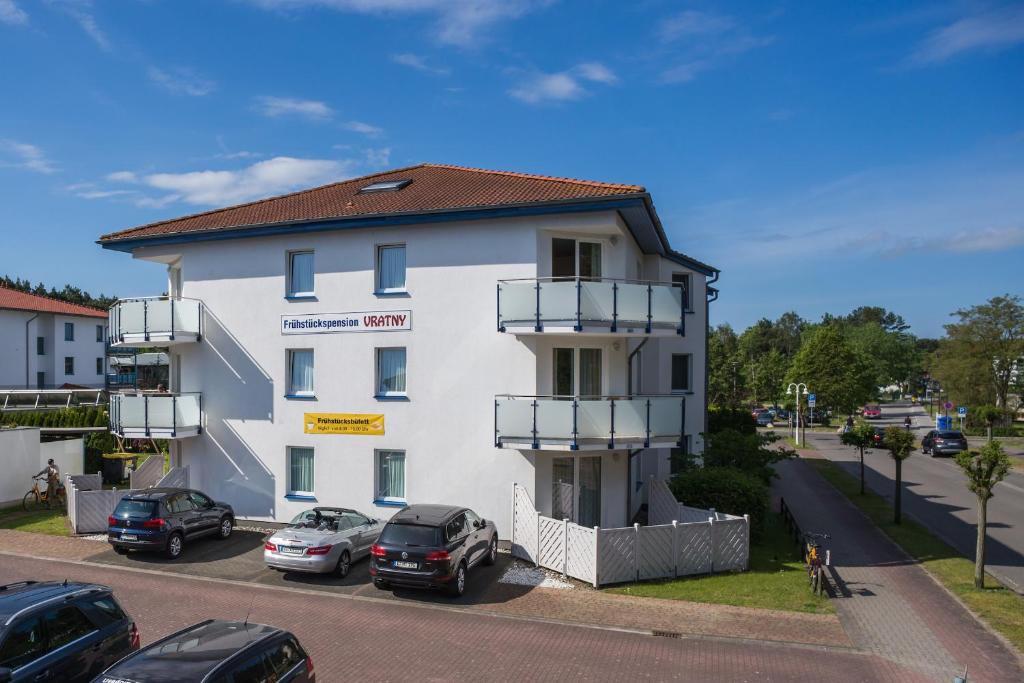 un edificio blanco con coches estacionados en un estacionamiento en Pension Maiglöckchen en Ostseebad Karlshagen