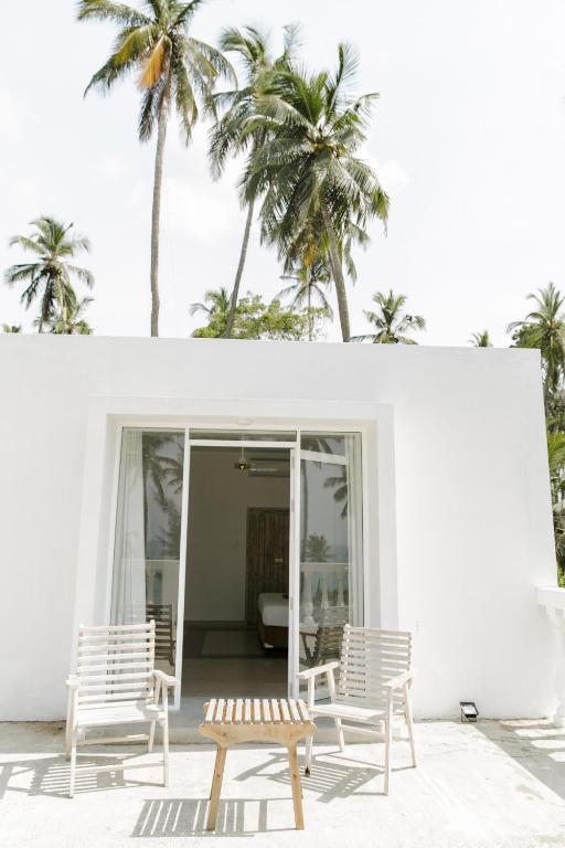 a white house with two chairs and palm trees at Nuga Eden Tangalle in Tangalle
