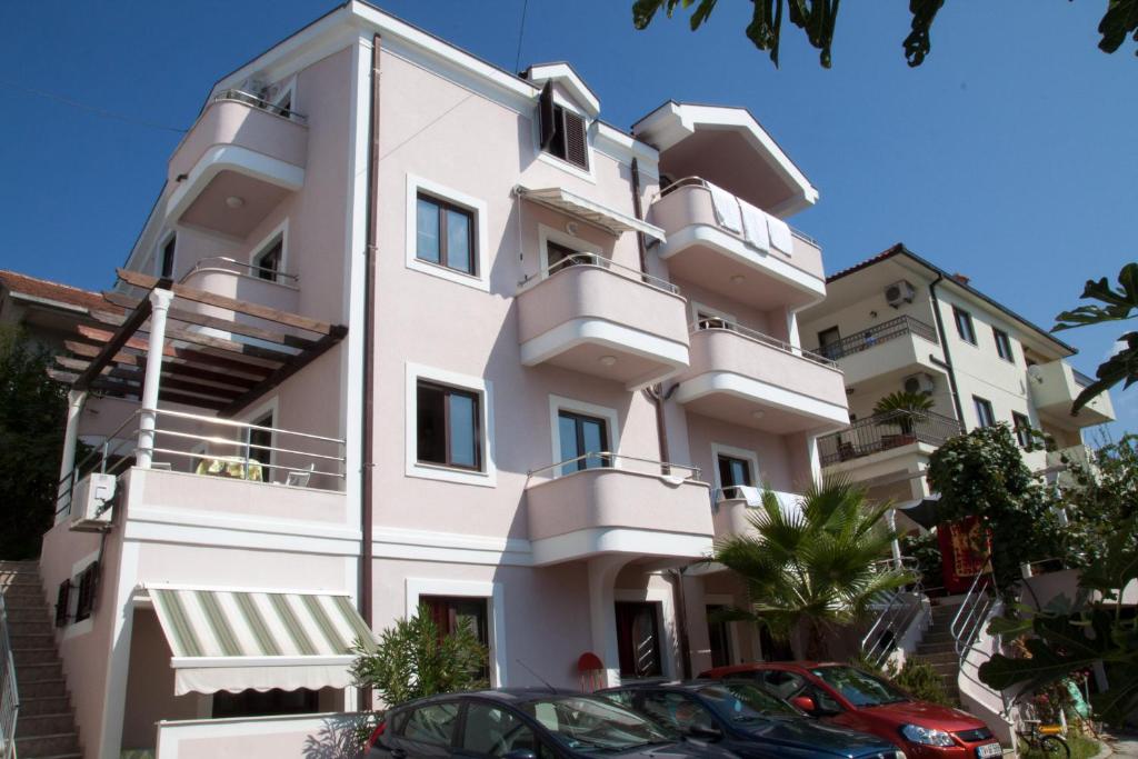 wysoki biały budynek z samochodami zaparkowanymi przed nim w obiekcie Apartments Maslina w mieście Herceg Novi