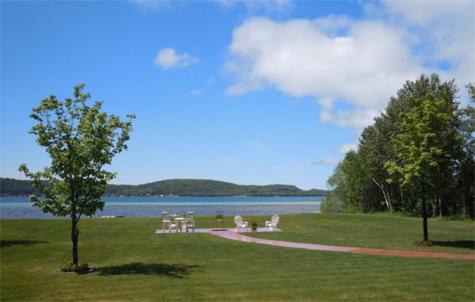 eine Gruppe von Tischen und Stühlen auf einem Feld in der Nähe eines Sees in der Unterkunft The Beach Inn Motel in Munising