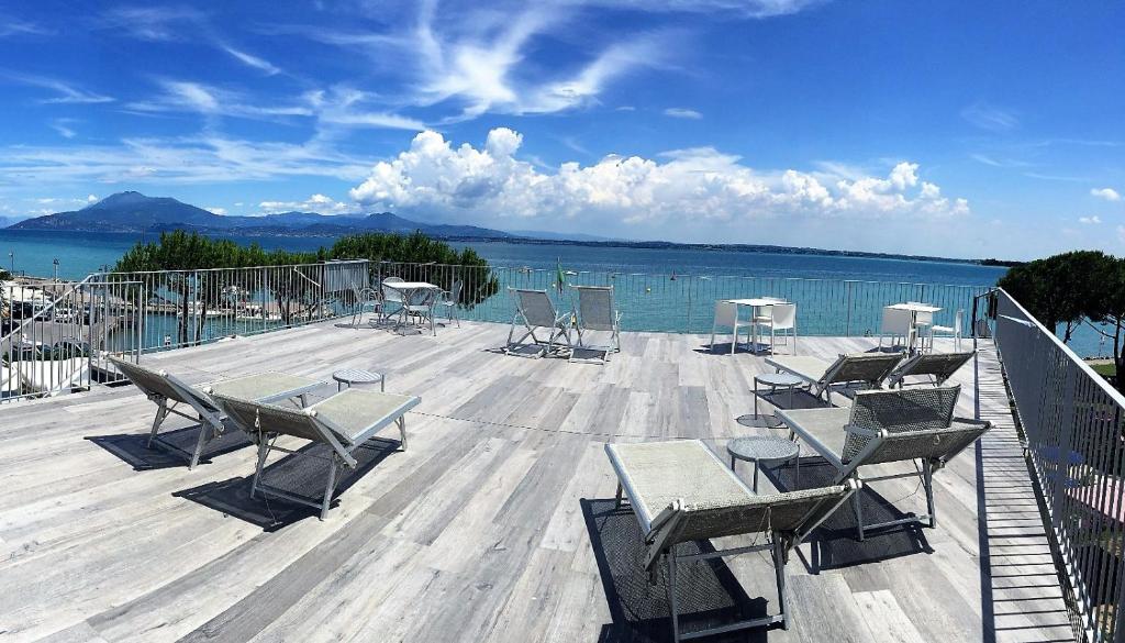 d'une terrasse avec des chaises et des tables offrant une vue sur l'eau. dans l'établissement Hotel Ca' Serena, à Sirmione