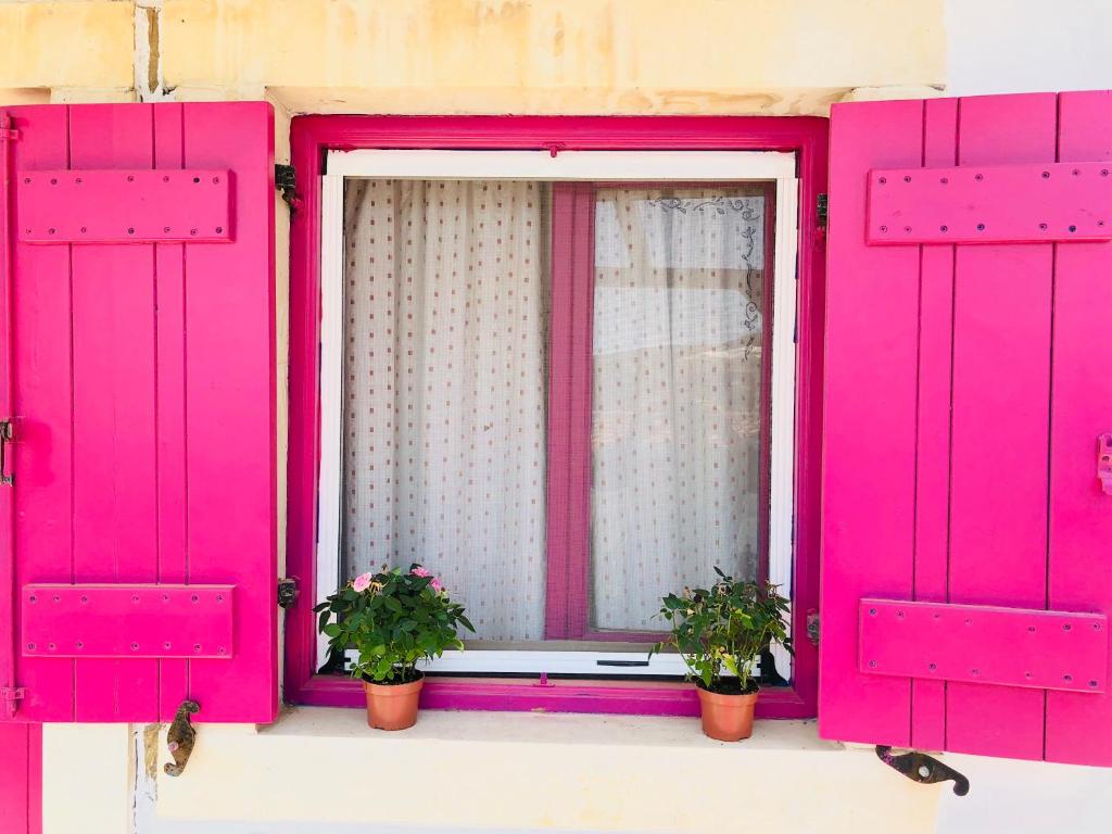 una ventana rosa con dos macetas. en Patras Apartments en Fourni Ikarias